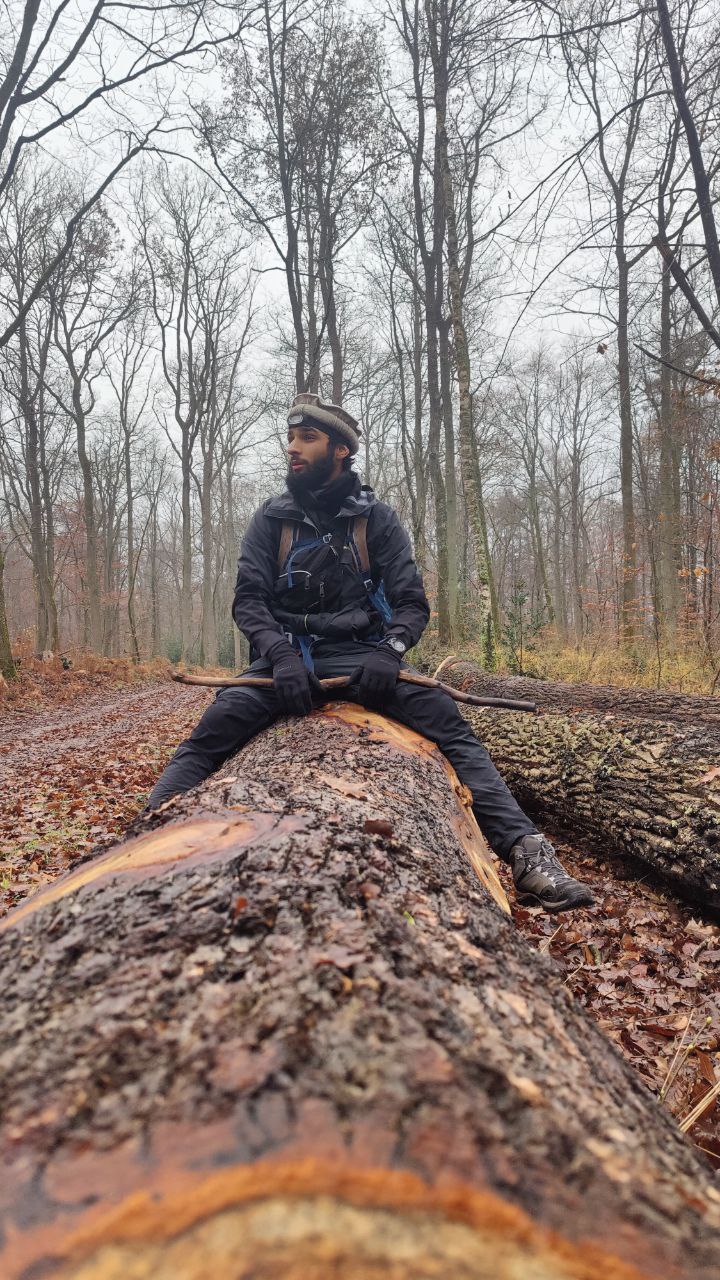 Ali Zaman assis sur un tronc d'arbre en forêt, en randonnée hivernale
