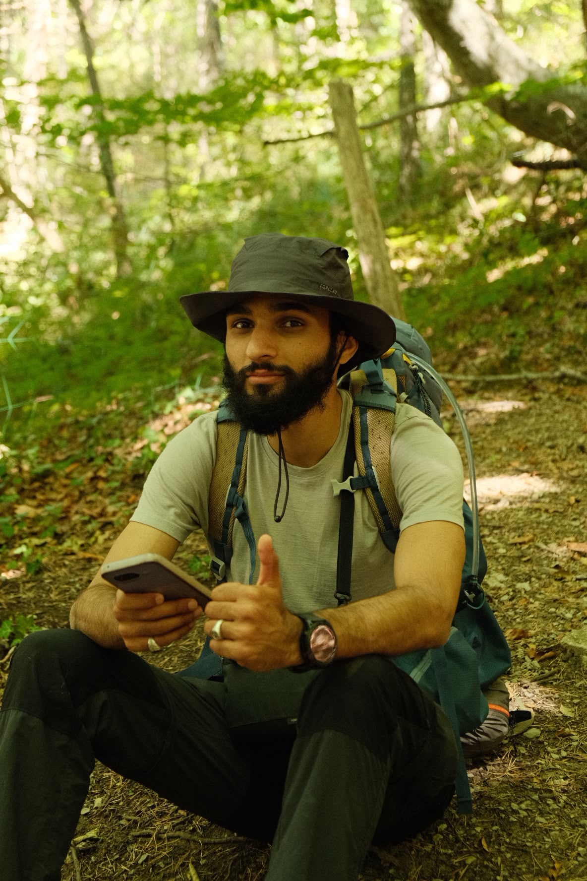 Ali Zaman en randonnée en forêt, pouce levé, sac à dos sur les épaules